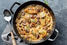 a skillet filled with chicken and mushrooms on top of a gray table next to a spoon