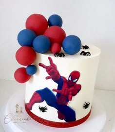 a spiderman themed cake with red, white and blue balloons on the top tier