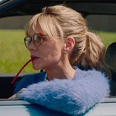 a woman with glasses sitting in the back seat of a car drinking from a straw