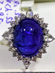 This tanzanite cabochon promise ring or anniversary ring is crafted in solid 18k white gold. The timeless and classic design of this beautiful ring will make your engagement or wedding unforgettable.SETTING :-Gross Weight: 4.054 gramsMetal: 18K White Gold(Customisable Also in Yellow Gold - No Extra Charge)Ring Size: 6 (Can be customisable) MAIN STONE :-Gem Type: Natural TanzaniteWeight: 9.50 CaratsShape: Oval CabochonColor: Rich Royal BlueClarity: VSADDITIONAL STONES :-(i) Stone Type: 100% Natur Formal Tanzanite Ring With Bezel Setting, Anniversary Sapphire Cabochon Ring In Platinum, Exquisite Tanzanite Rings, Brilliant Cut Tanzanite Gemstones, Anniversary Sapphire Cabochon Ring, Luxury Round Tanzanite Gemstones, Exquisite Tanzanite Ring For Anniversary, Luxury Tanzanite Gemstones, Exquisite Tanzanite Anniversary Ring