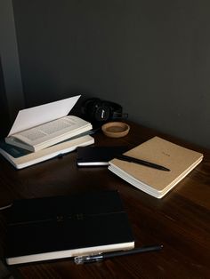 three notebooks and two pens are sitting on a table next to an open book