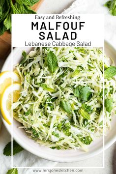 a white plate topped with shaved cabbage salad next to sliced lemons and mint leaves