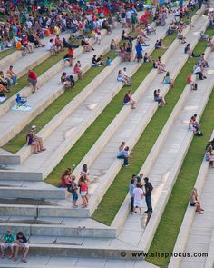 many people are sitting and standing on the steps in front of some stairs with grass