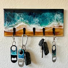 four keys hanging from hooks on a wall next to a beach and ocean wave painting