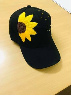 a black hat with a yellow sunflower on it sitting on top of a wooden table