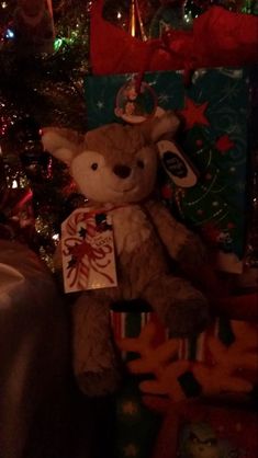 a brown teddy bear sitting in front of a christmas tree