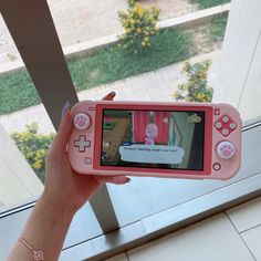 a person holding up a pink nintendo wii game controller in front of a glass window