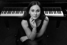 a woman sitting in front of a piano with her hands on her chin and looking at the camera