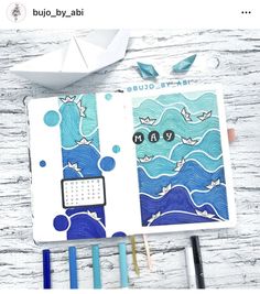 an open notebook with blue and white designs on it, next to pens and scissors