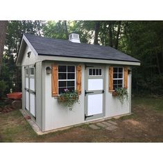 a small shed with windows and shutters on the side, in front of some trees