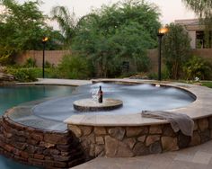 a pool with a fountain in the middle of it next to a stone wall and trees