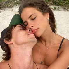 a man and woman laying on top of each other in the sand with their noses close together