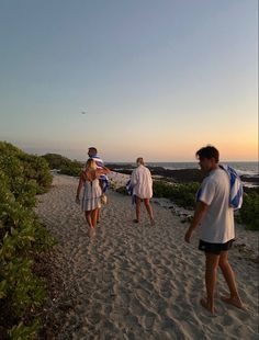 several people walking on the beach at sunset