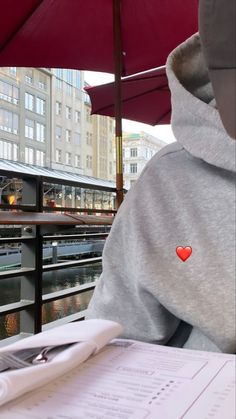 a person in a hoodie sitting at a table with an umbrella over their head