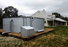 a large metal tank sitting in the middle of a field next to a house and trees