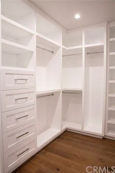 an empty walk in closet with white shelves and drawers