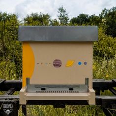 a yellow and white box sitting on top of a wooden bench in the grass with trees behind it