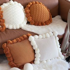 three decorative pillows sitting on top of a brown couch next to a white sheepskin rug