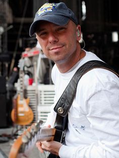 a man holding a guitar in his right hand and wearing a hat on the other