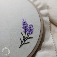 a close up of a purple flower embroidered on a white piece of cloth with lace