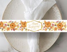 a white plate topped with a napkin covered in autumn leaves and pumpkins next to a happy thanksgiving sign