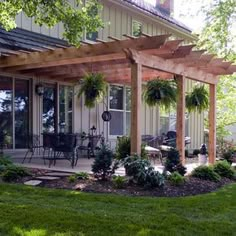 an outdoor patio covered with plants and potted trees in front of a large house