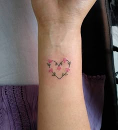 a woman's arm with a heart shaped tattoo on her left wrist and pink flowers in the middle