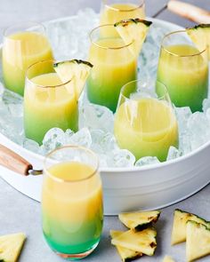 several glasses filled with drinks sitting on top of an ice tray next to slices of pineapple