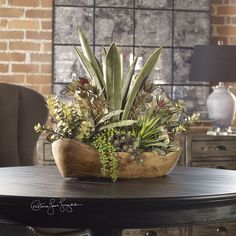 a wooden bowl filled with lots of plants on top of a table next to a chair