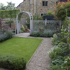 a small garden with lots of flowers and plants around it, including an arch in the middle