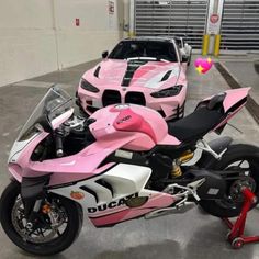 a pink and white motorcycle parked next to a car in a garage with other cars