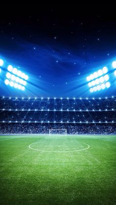 an empty soccer field at night with bright lights on the stands and fans in the stands