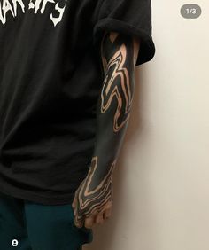 a man with tattoos on his arm standing next to a wall