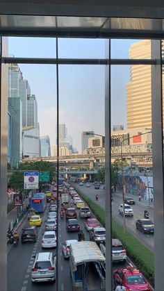 a city street filled with lots of traffic next to tall buildings in the distance, as seen from a large window