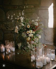 flowers and candles are arranged on a table in front of a brick wall with windows