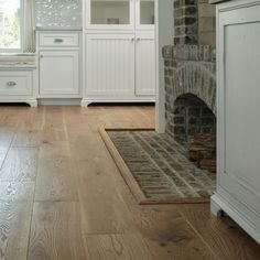 a kitchen with white cabinets and wood flooring next to a brick oven in the center