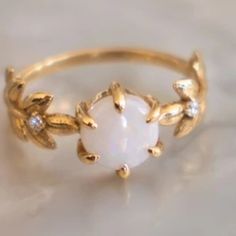 a gold ring with a white stone surrounded by leaves