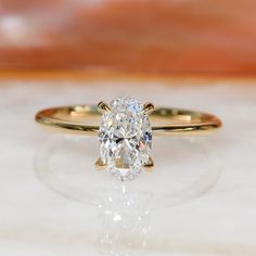 an oval cut diamond sits on top of a gold band and is flanked by a thin band