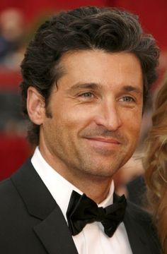 a man in a tuxedo smiles at the camera while standing next to a woman