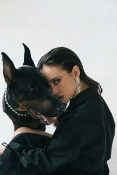 a woman is hugging her dog in front of a white wall and she has her head on the back of the dog's neck