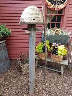 an old fashioned bird feeder in front of a red building with potted plants on it