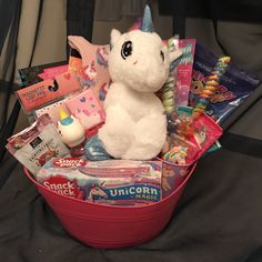 a stuffed unicorn sitting in a red basket filled with candy and other items on a bed