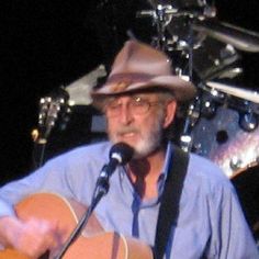 a man with a hat and glasses playing an acoustic guitar in front of a microphone