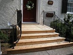 a front porch with steps leading up to the door and wreath hanging on the wall