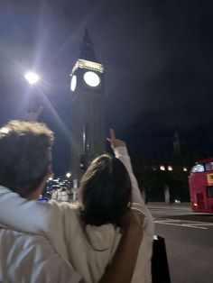 a man and woman standing in front of a clock tower with their arms around each other