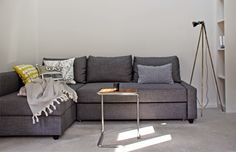 a living room with a gray couch and some pillows on the floor next to a book shelf