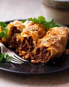 a black plate topped with meat and cheese burritos next to a silver fork