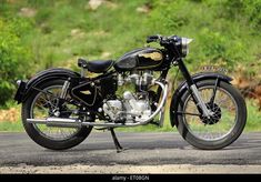 an old black motorcycle parked on the side of the road in front of some trees