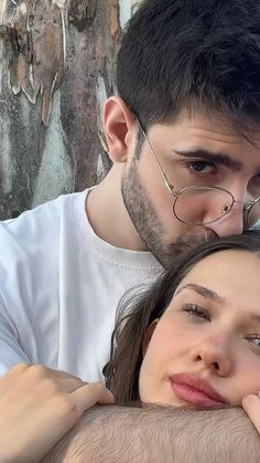 a man and woman standing next to each other in front of a tree with their eyes closed