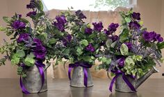 three metal watering cans with purple flowers in them